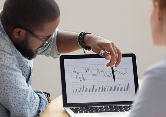 A man showing a chart on a laptop screen to someone else