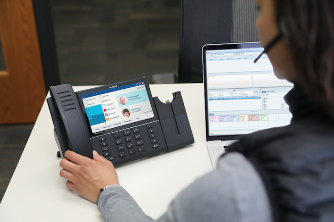 Someone working on a desk with the Mitel phone and a laptop