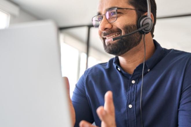 Man talking with his headset on and facing his laptop