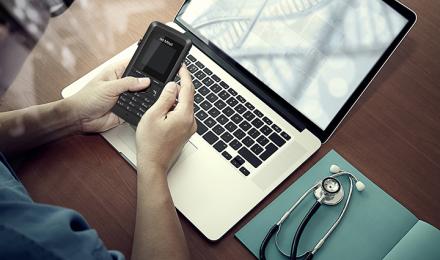 A guy looking at his phone on top of his laptop