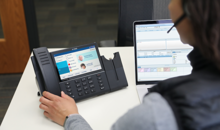 Someone working on a desk with the Mitel phone and a laptop