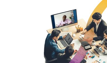 People on meeting around a table with someone on video meeting in a monitor