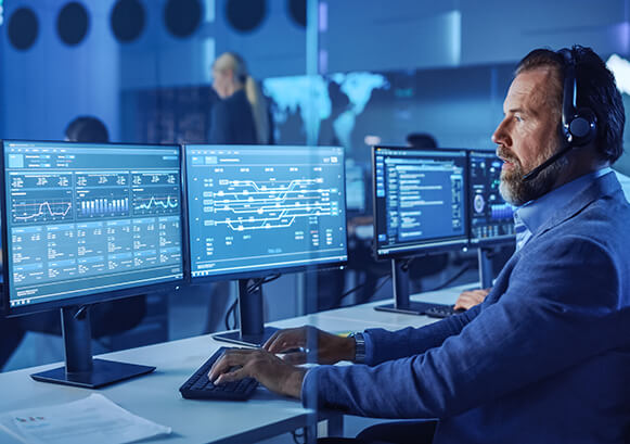 A man in front of many monitors with charts on it