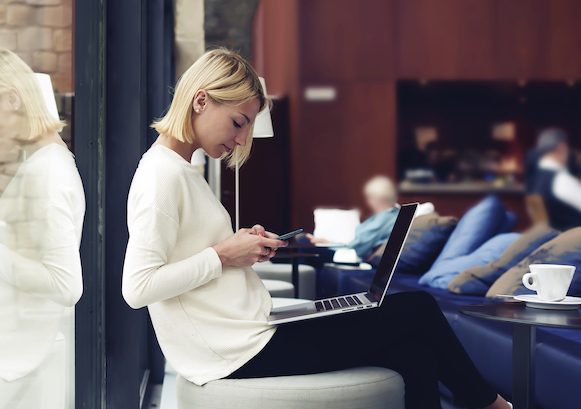 A woman working on a laptop, seating on a chair with a coffee in front of her