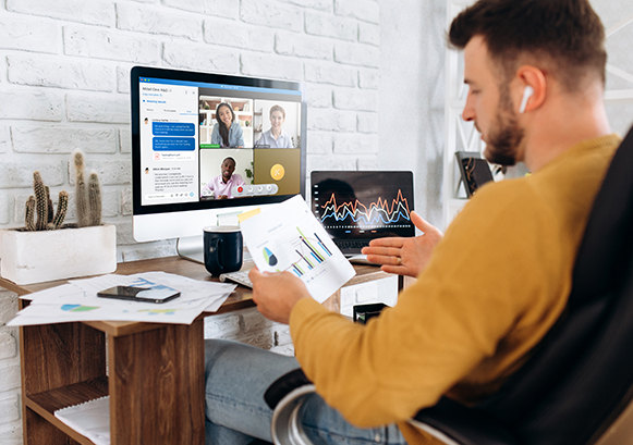 A guy at his desk, doing a video conference, but also looking at a paper with a graph in front of him
