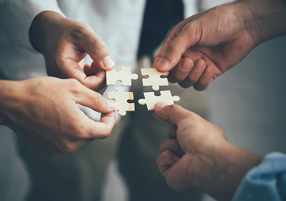 Four people putting together four puzzle pieces