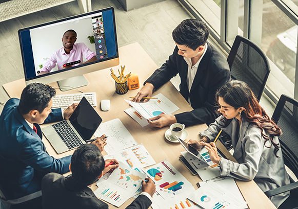 People collaborating around a table with someone a video meeting