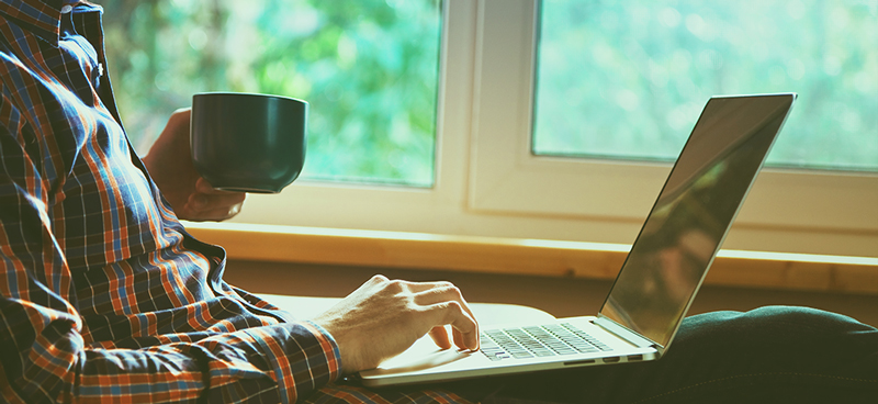 Someone holding a coffee cup in front of his laptop