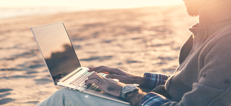 A guy looking at a laptop by the water