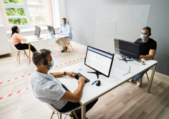 People working in desks separated by two lines and wearing masks