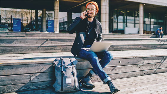 A guy on a phone, with his laptop on his lap, in a train station