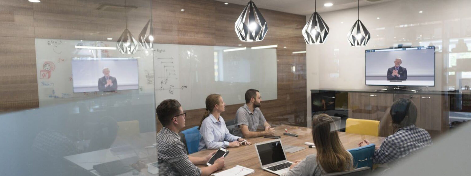 People in a video conferring in a meeting room, looking at a monitor