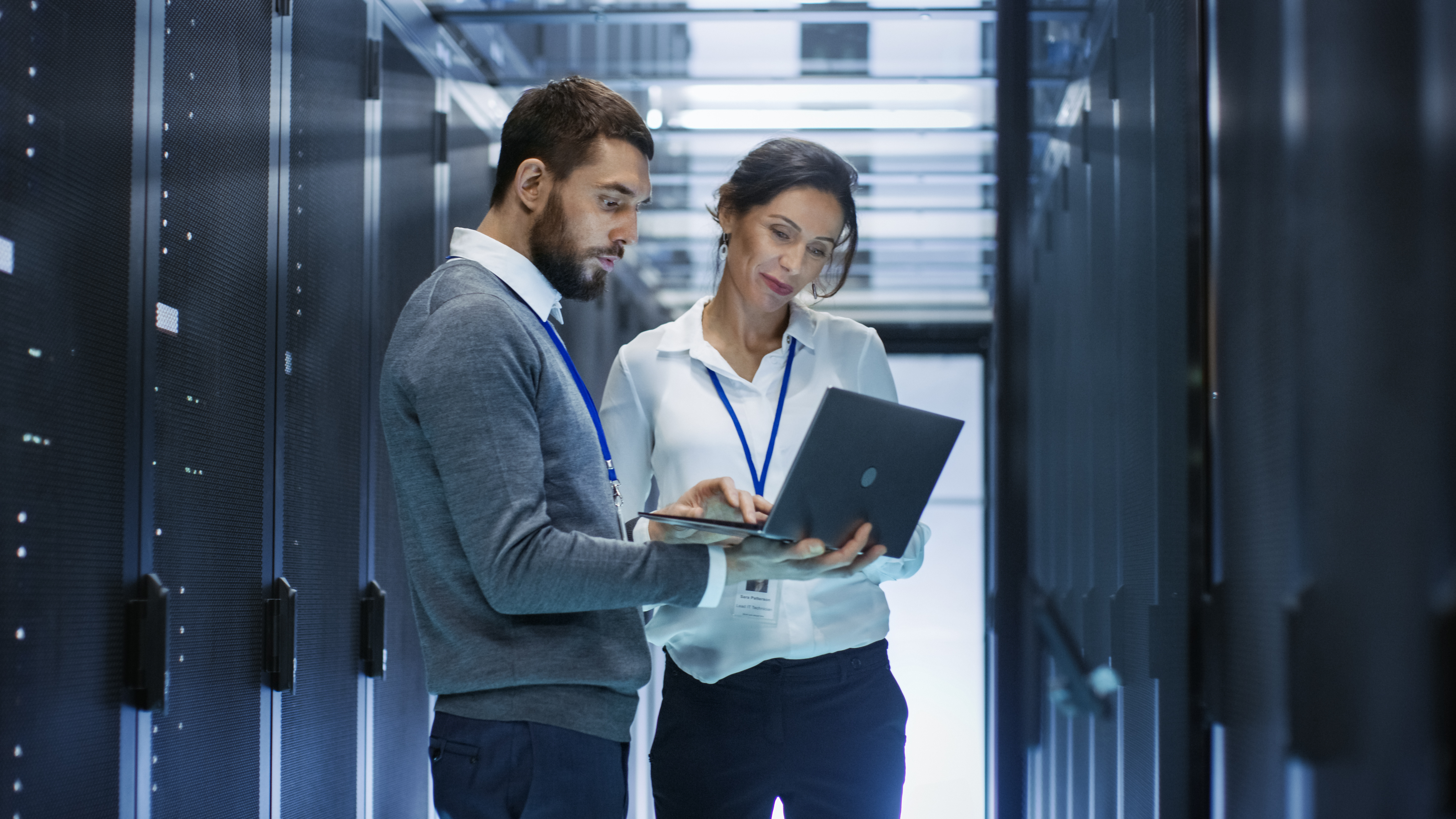 two persons looking at a laptop in a server room