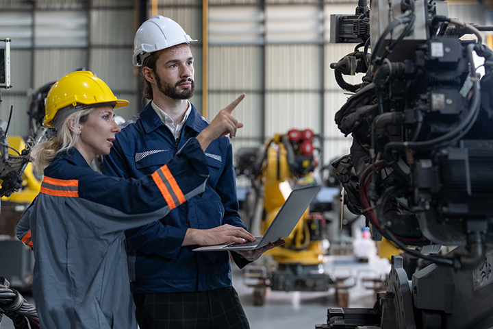 Two people in safety gear pointing manufacturing