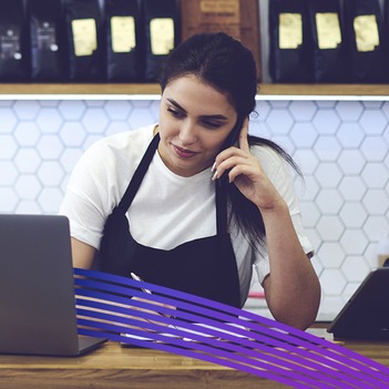 Retail store employee on a call at the counter while using a laptop