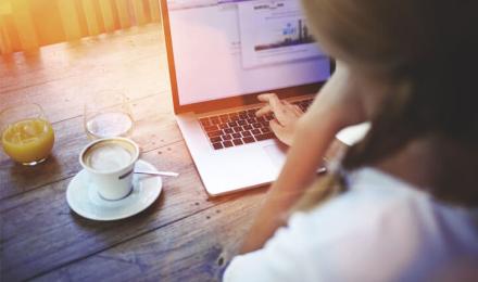 A woman in front of her laptop with a coffee on the side