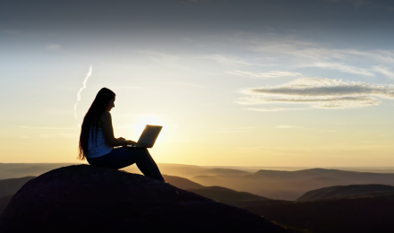 A woman looking at her laptop during the sunset 